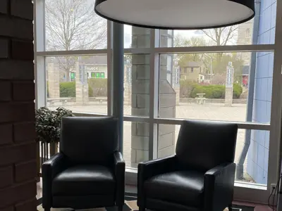 two reclining chairs in black under a big black circle light, placed in front of floor to ceiling windows