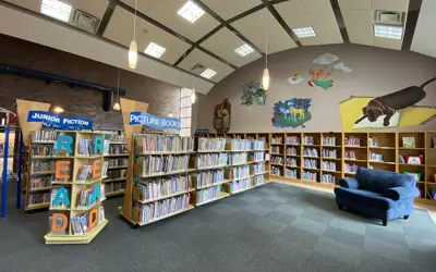 rows of children's book shelves, big comfy blue chair on rug with open seating in front of it